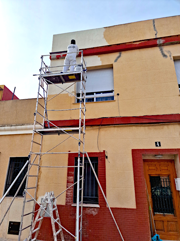 Empresa de pintores de fachadas realizando rehabilitación de exteriores y pintado de muros en viviendas con andamiaje profesional.