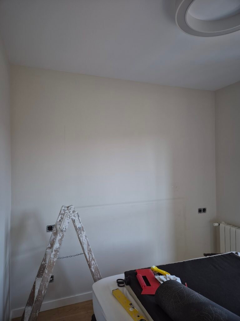 Servicio de pintores profesionales de interiores realizando la preparación y alisado de paredes en un dormitorio residencial.