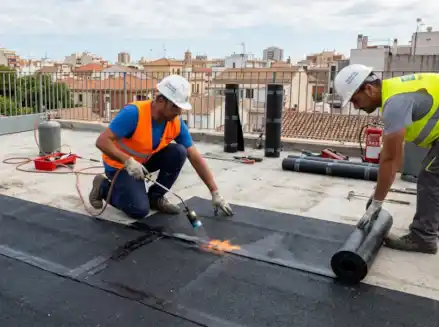 Operarios realizando la impermeabilización de terrazas con tela asfáltica mediante soplete de gas en una azotea urbana.