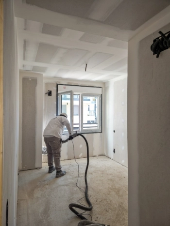 Pintores de obra nueva preparando superficies y aspirando polvo en una estancia en construcción.