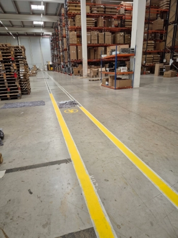 Señalización de suelos industriales con líneas amarillas y paso peatonal en un almacén logístico.