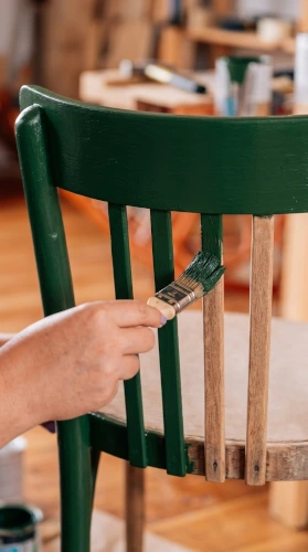 Pintor de muebles de madera aplicando pintura verde con brocha en el respaldo de una silla