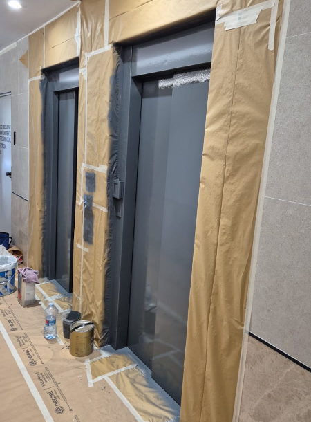 Trabajo de pintores de ascensores de comunidades de vecinos protegiendo el portal y pintando puertas metálicas en gris