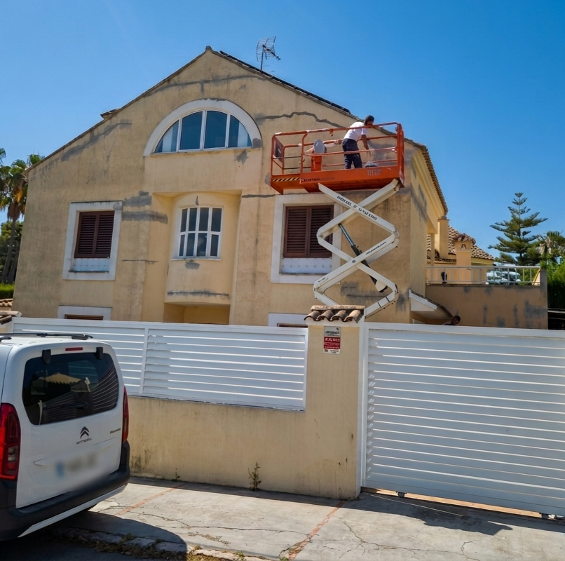 pintores de chalets trabajando en la reparación de grietas y pintura de fachada con plataforma elevadora